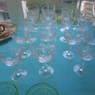 Collection of vintage cut crystal wine glasses and goblets with starburst and crisscross patterns, displayed on a blue tablecloth.
