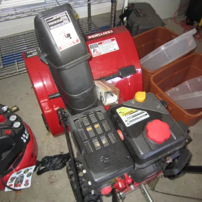 Craftsman gas-powered snowblower with a red body and black engine housing, shown alongside a red pancake air compressor.