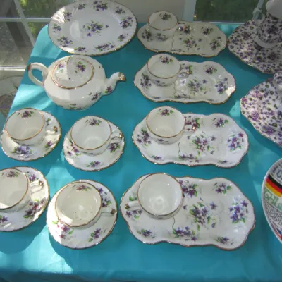 Vintage porcelain tea set decorated with purple violets and gold trim, including a teapot, cups, saucers, and snack plates.
