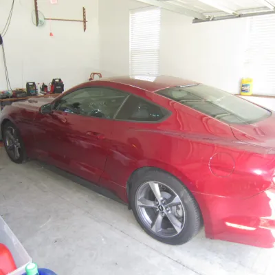 Modern Ford Mustang coupe in metallic red, parked inside a garage alongside various tools and storage containers.