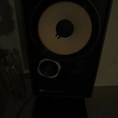 Vintage JBL L100 Century speaker with a white woofer cone, housed in a walnut cabinet and mounted on a black stand.