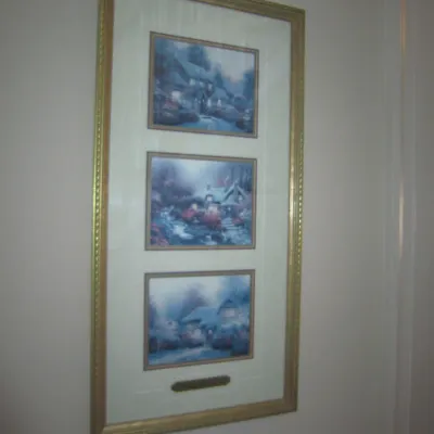 Thomas Kinkade framed triptych print featuring three cottage scenes, presented in a gold-finished frame with a white mat.