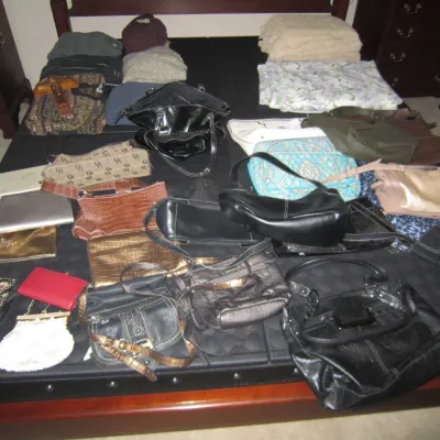 Large collection of assorted women's handbags, purses, and clutches in various styles, colors, and materials, displayed on a bed.