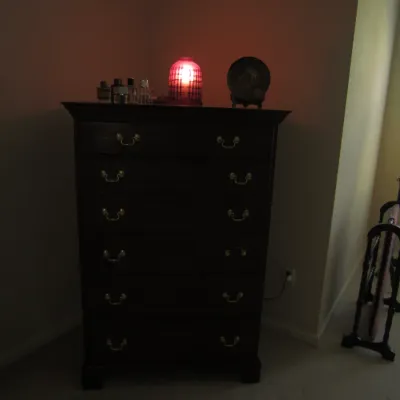 Traditional dark wood tallboy chest of drawers featuring brass bail pulls, styled with a small red lamp and decorative items on top.