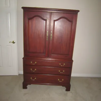 Traditional cherry wood armoire featuring a two-door upper cabinet with arched panels and three lower drawers with brass batwing pulls.