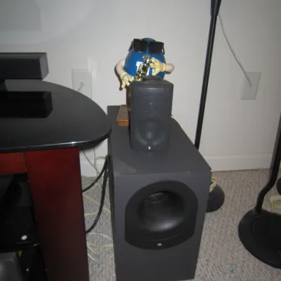 JBL subwoofer and satellite speaker paired with a novelty blue M&M saxophone-playing character dispenser.