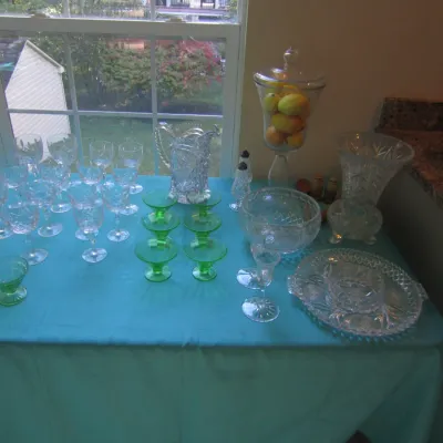 Assortment of vintage glassware, including clear cut-glass goblets, a pitcher, a lidded apothecary jar, and green depression glass...