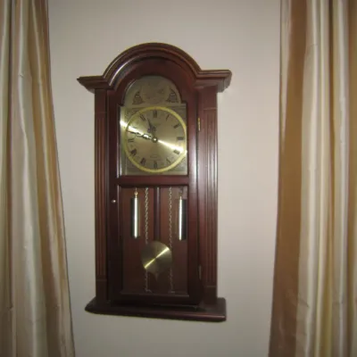 Traditional Howard Miller wall clock in a dark wood case, featuring a brass dial with Roman numerals, exposed weights, and a pendulum.
