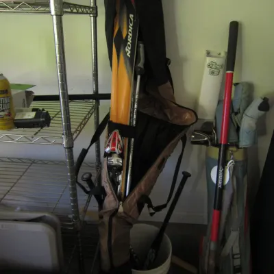 Nordica downhill skis with bindings and poles in a zippered carrying bag, shown alongside golf clubs and garage storage items.