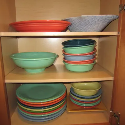 Assorted Fiesta ceramic dinnerware, including plates, bowls, and serving dishes in various signature colors, organized inside a wooden...