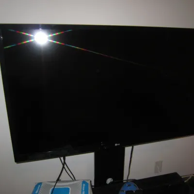 LG flat-screen television mounted on a black stand, showing a glossy screen with a camera flash reflection.