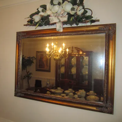 Large rectangular wall mirror featuring an ornate, antiqued gold-finished frame with molded corner details, topped with a decorative faux...