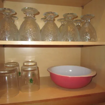 Vintage glassware collection including textured clear goblets, holiday-themed drinking glasses, and a pink Pyrex Cinderella mixing bowl...