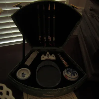 Chinese calligraphy set in a fan-shaped presentation box, including brushes, an inkstone, a brush rest, and porcelain accessories.