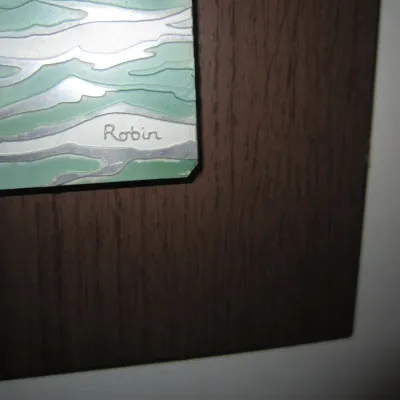 Close-up detail of a mid-century modern enamel-on-copper artwork signed "Robin," mounted on a dark wood backing.
