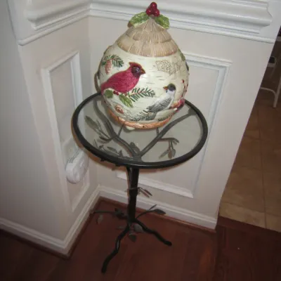 Fitz and Floyd winter bird ceramic cookie jar displayed on a small round glass-top accent table with a metal branch-style base.