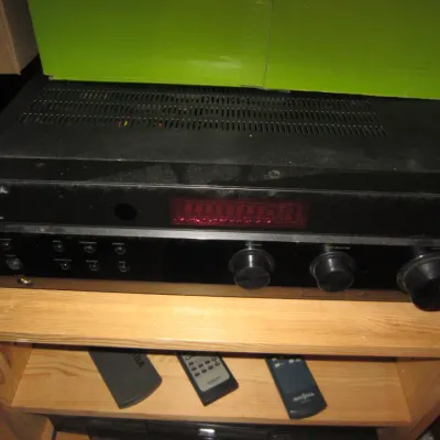 Insignia stereo receiver in black finish, showing some dust and wear, displayed on a wooden shelf with remote controls below.