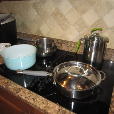 Assorted kitchen cookware including stainless steel pots and pans, a light blue enamel pot, and a tall stainless steel stockpot with...