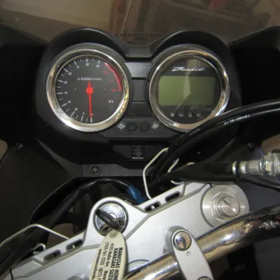 Instrument cluster and handlebars of a Suzuki Bandit motorcycle, showing the analog tachometer and digital display.
