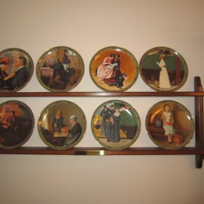 Set of eight Norman Rockwell collector plates displayed on a two-tier wooden wall shelf.