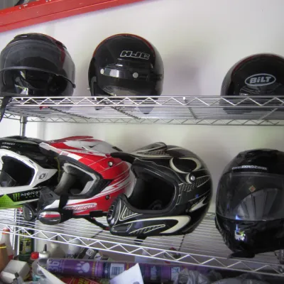 Collection of motorcycle and motocross helmets, including brands like HJC, Bilt, and O'Neal, displayed on a wire shelving unit.