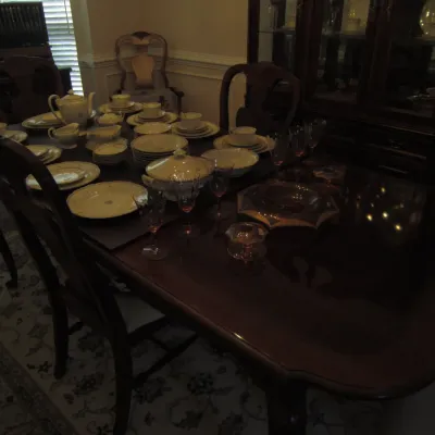 Traditional mahogany dining table and chairs set, featuring a polished wood tabletop styled with a vintage porcelain dinnerware set and...