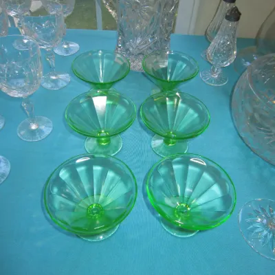 Set of six vintage green uranium glass sherbet cups with a paneled design, displayed alongside clear cut glass stemware and a pitcher.