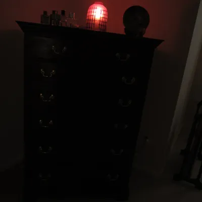 Traditional dark wood tallboy chest of drawers with brass batwing pulls, styled with a glowing red accent lamp and decorative items on top.