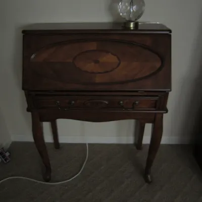 Vintage mahogany slant-front secretary desk featuring a decorative oval wood inlay on the drop-down lid, a single drawer with brass...