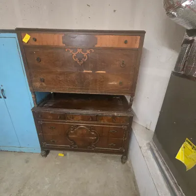 Antique two-piece wooden dresser set featuring ornate carved details and metal ring pulls, showing significant wear and veneer damage,...