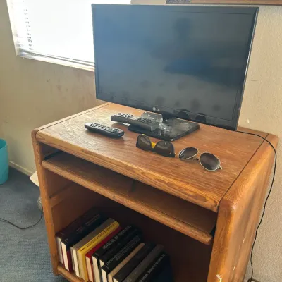 LG flat-screen television with remotes, resting on a vintage oak media cart with a pull-out shelf and lower storage compartment,...