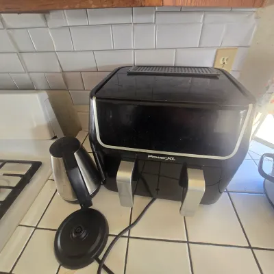 PowerXL dual-basket air fryer in black and silver finish, shown alongside a stainless steel electric kettle with its heating base. Buy It...