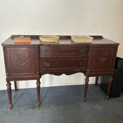 Antique dark wood sideboard with fluted legs and metal hardware, showing significant surface wear and distressing, available for a...