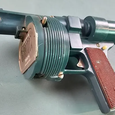 Vintage Hubley Atomic Disintegrator cap gun, featuring a metallic green finish and textured brown grip panels, showing some light wear...