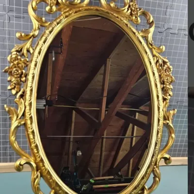 Vintage ornate oval wall mirror featuring a heavily detailed, gilded gold-finished frame with scrollwork and floral motifs.