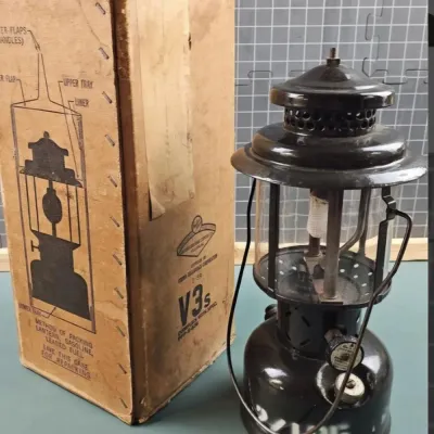 Vintage military-style Coleman gasoline lantern with its original cardboard shipping box, showing some wear and stenciled markings.