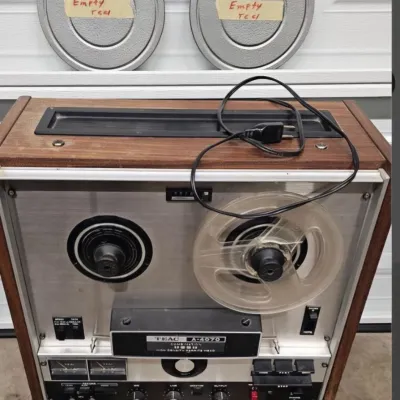 Vintage TEAC A-4070 reel-to-reel tape deck with wood cabinet, accompanied by two empty metal reels.