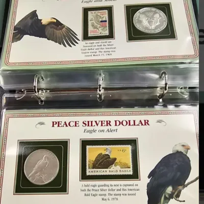 Two commemorative coin and stamp display panels in a binder, featuring a Silver Eagle Dollar with a 1969 American Legion stamp and a...