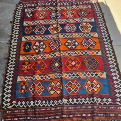 Vintage hand-woven flatweave Kilim rug featuring vibrant geometric patterns in red, blue, orange, and white with fringed ends.