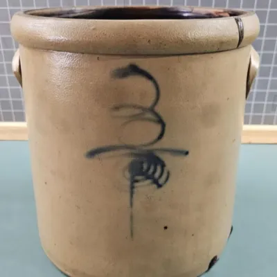 Antique salt-glazed stoneware crock with cobalt blue hand-painted decoration and molded ear handles, showing some wear and minor cracking...