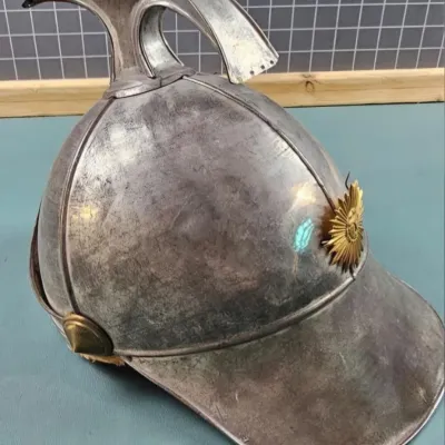 Vintage metal firefighter helmet featuring a prominent top crest and a brass sunburst emblem on the front.