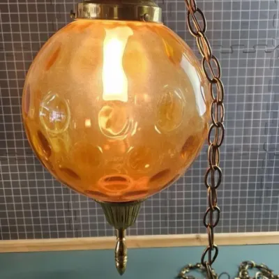Mid-century modern amber glass swag lamp featuring a thumbprint pattern globe, brass hardware, and a hanging chain.