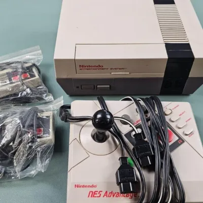 Vintage Nintendo Entertainment System (NES) console, accompanied by an NES Advantage joystick controller and two standard controllers...