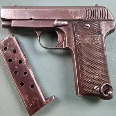 Vintage semi-automatic pistol with textured grip panels and a lanyard loop, shown with its detached magazine.