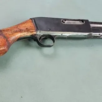 Vintage pump-action rifle featuring a worn wooden stock and ribbed forend, showing signs of age and use.