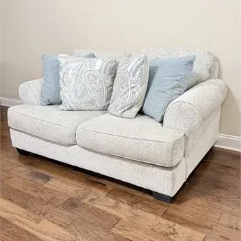 Sale Photo Thumbnail #17: Contemporary light gray upholstered loveseat featuring rolled arms, paired with four coordinating throw pillows in solid blue and paisley patterns.
