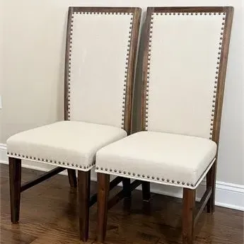 Sale Photo Thumbnail #38: Pair of contemporary high-back dining chairs featuring off-white fabric upholstery, dark wood frames, and decorative brass nailhead trim.