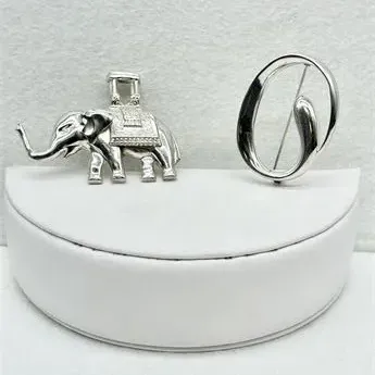 Sale Photo Thumbnail #56: Two sterling silver brooches, featuring a detailed elephant with a howdah and a modern minimalist abstract oval design.
