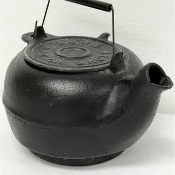 Sale Photo Thumbnail #41: Vintage cast iron tea kettle with a wire bail handle and a black wood grip, featuring embossed lettering on the lid.