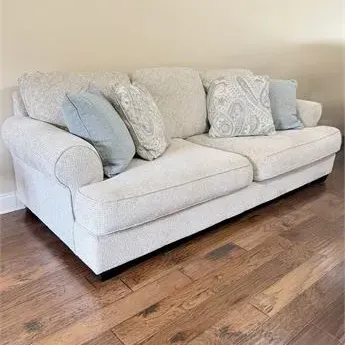 Sale Photo Thumbnail #11: Contemporary light beige upholstered sofa with rolled arms, featuring a mix of solid light blue and paisley patterned accent pillows.